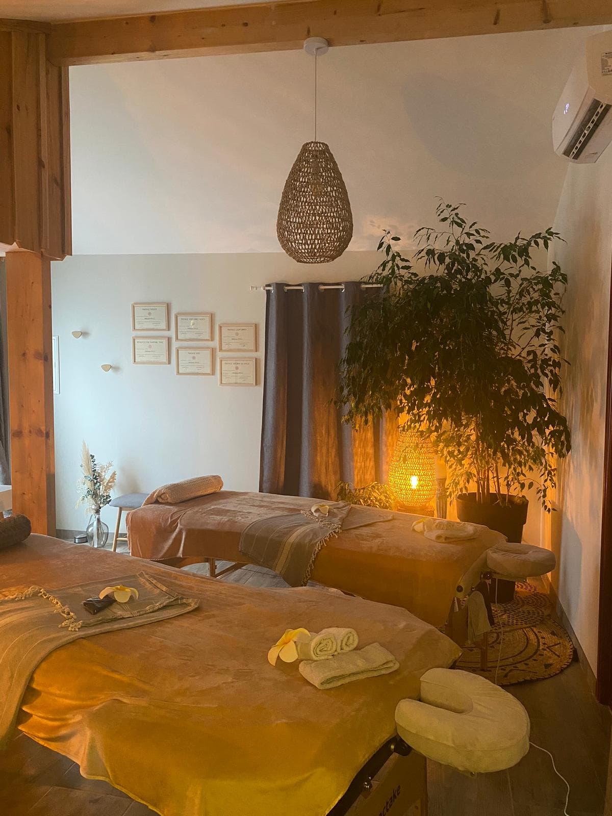 Deux tables de massage drapées de velours camel, fleurs de frangipanier et lampe en rotin allumée